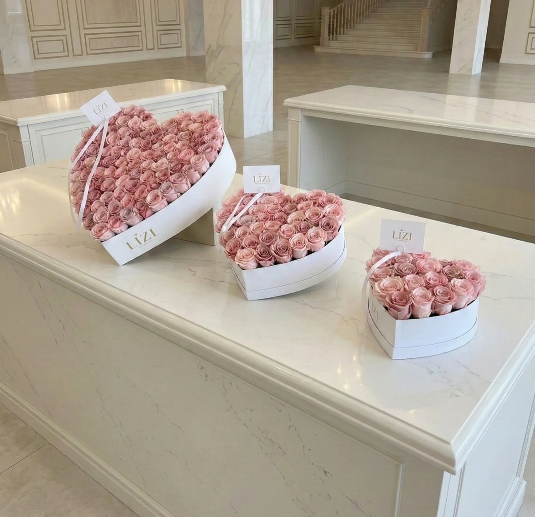 Tres cajas blancas en forma de corazón con rosas rosadas sobre un mostrador